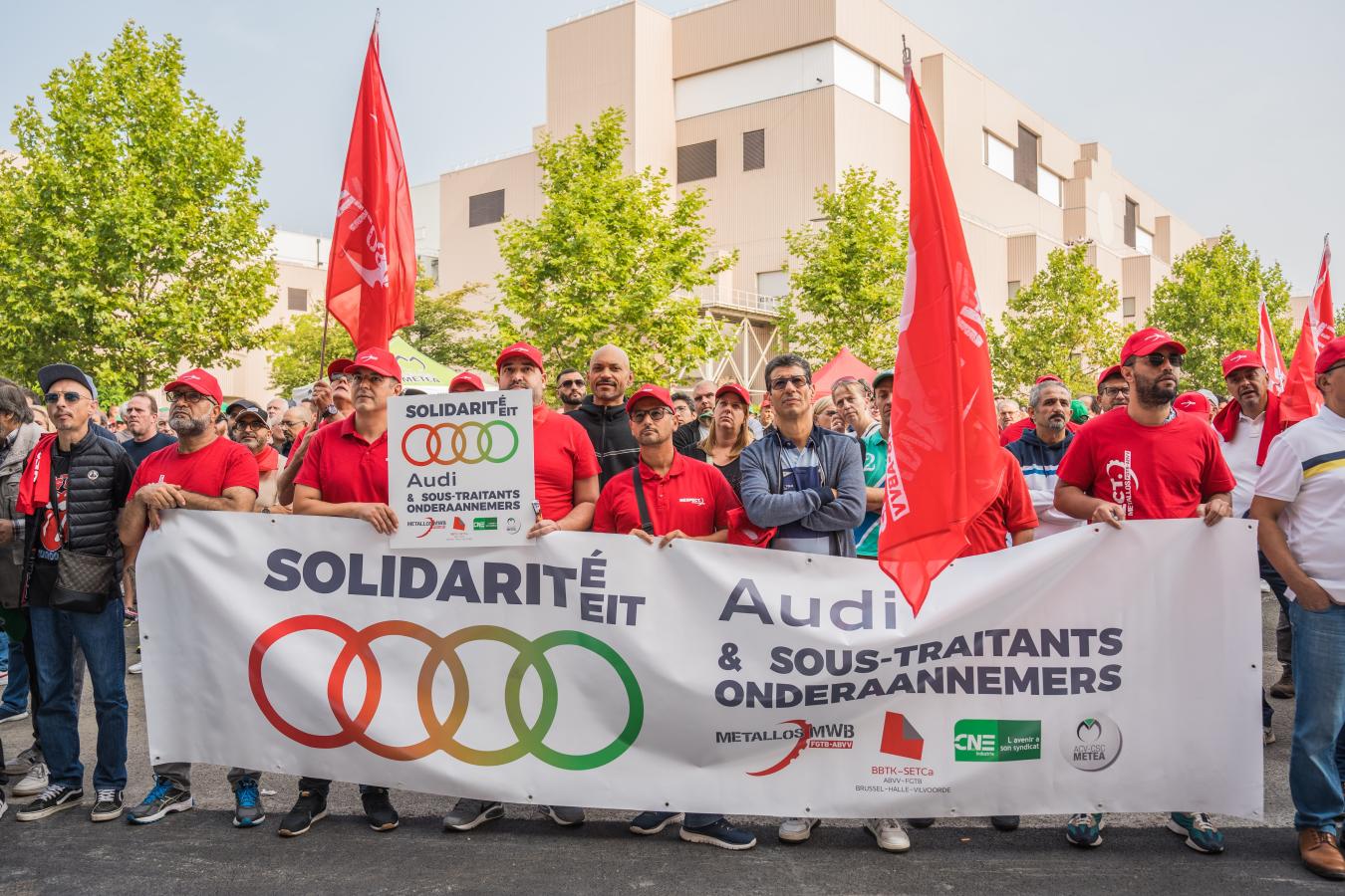 Des travailleurs rassemblés devant l'usine de Audi Brussels avec une banderole